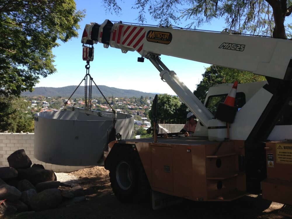 Crane lifting a concrete ring into position on a hillside site
